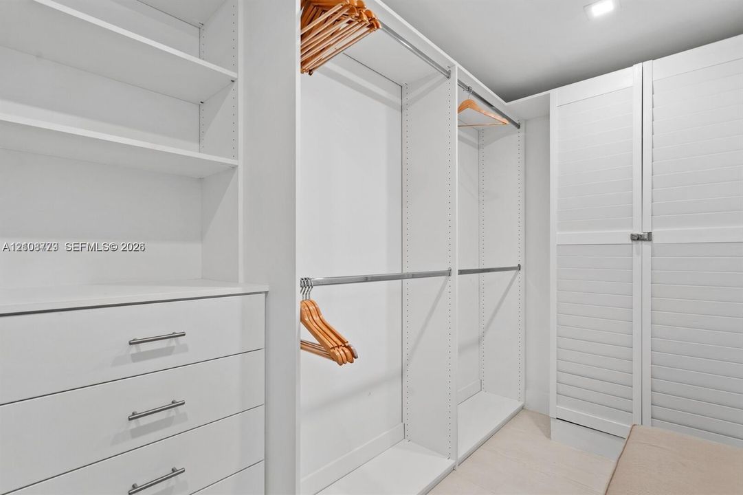 Walk-in closet featuring white built-in shelving, integrated dresser drawers, dual-tier hanging rods, and louvered cabinet doors