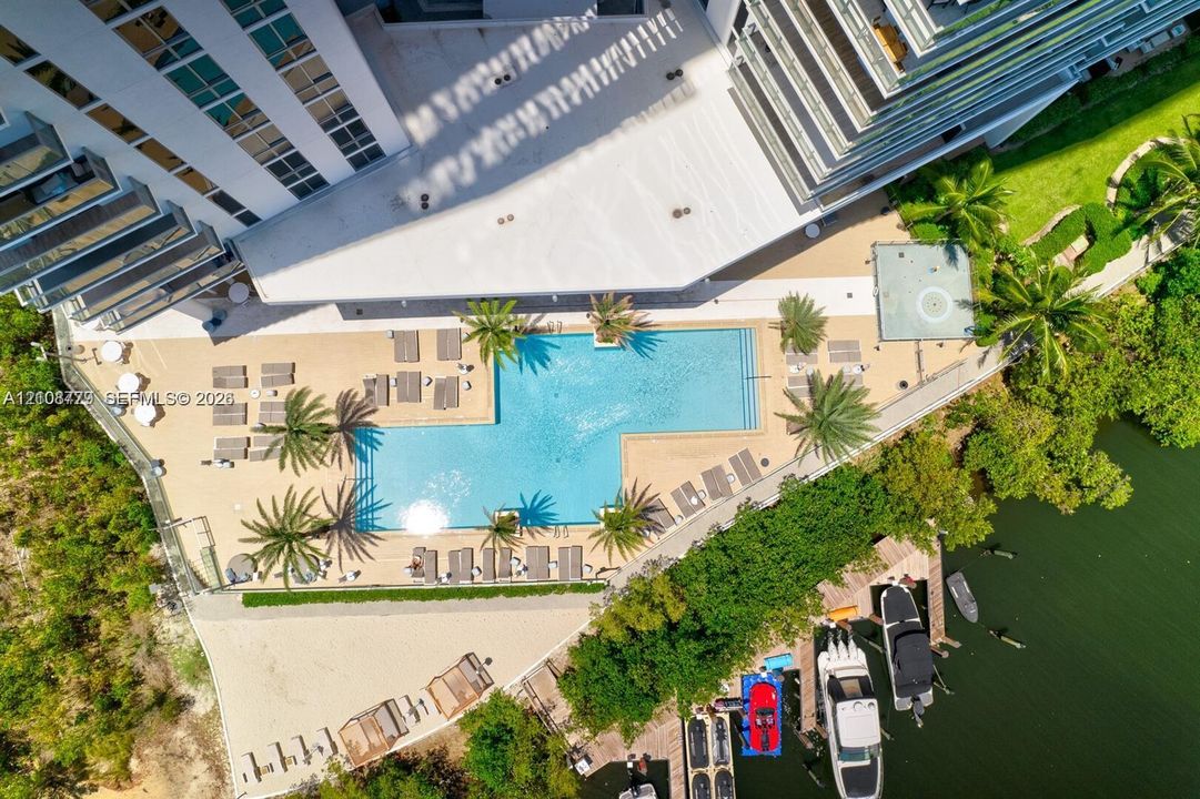 Aerial perspective featuring a swimming pool, paved sundeck, tropical landscaping, and private boat slips along the shoreline