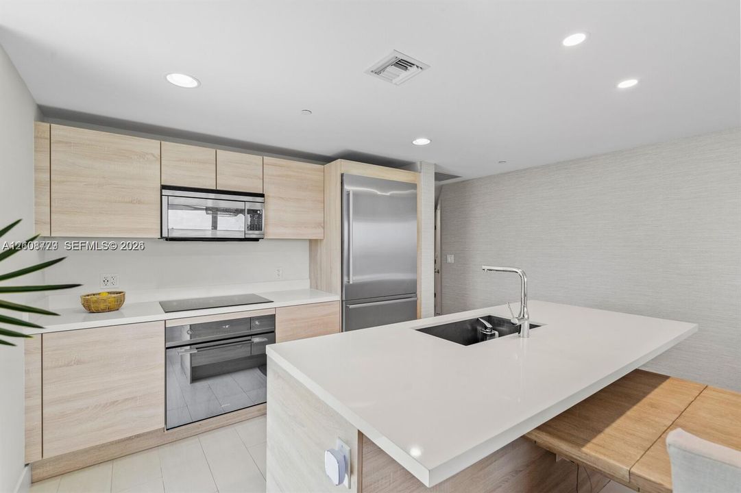 Kitchen featuring light wood-finish cabinetry, quartz countertops, a central island with an undermount sink and chrome faucet, recessed lighting, and stainless-steel appliances