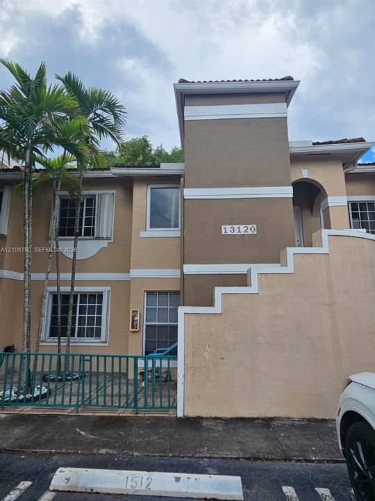 Stucco exterior with multi-level architectural detailing, decorative white trim, and a paved front patio enclosed by metal fencing