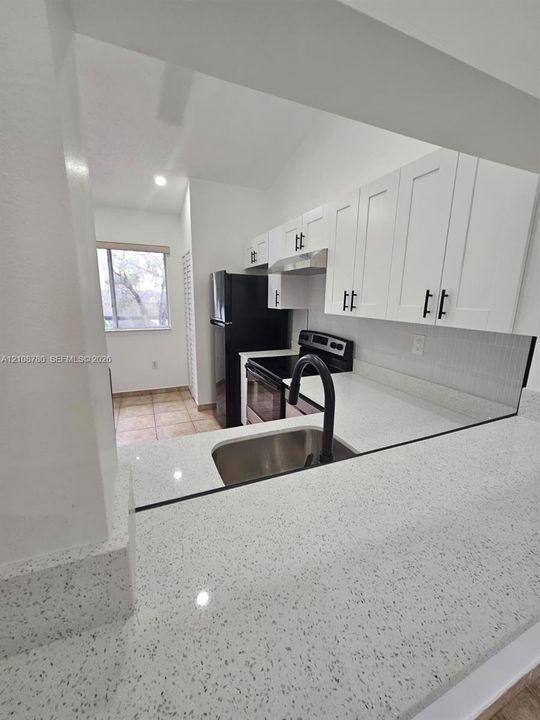 Kitchen featuring white shaker-style cabinetry, quartz countertops, a stainless steel undermount sink, a matte black high-arch faucet, and a subway tile backsplash