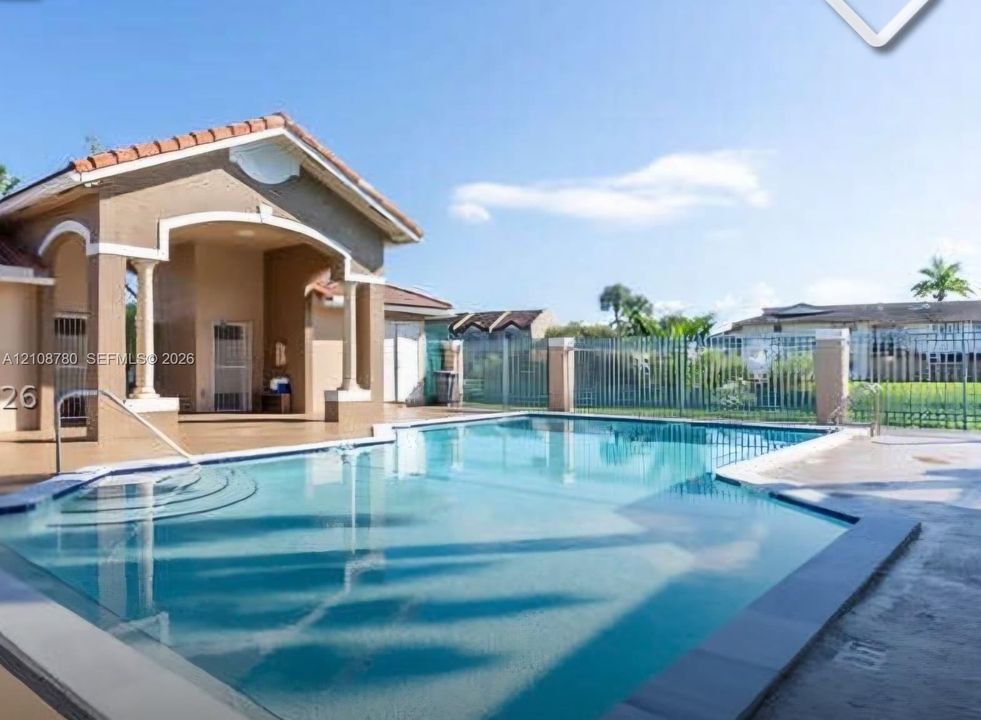 Swimming pool with integrated steps, covered patio structure with architectural columns, and perimeter metal fencing