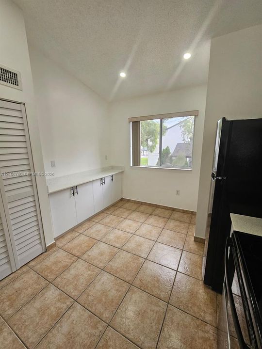 Vaulted ceiling with recessed lighting, tile flooring, built-in lower cabinetry with solid-surface countertops, and a louvered-door closet