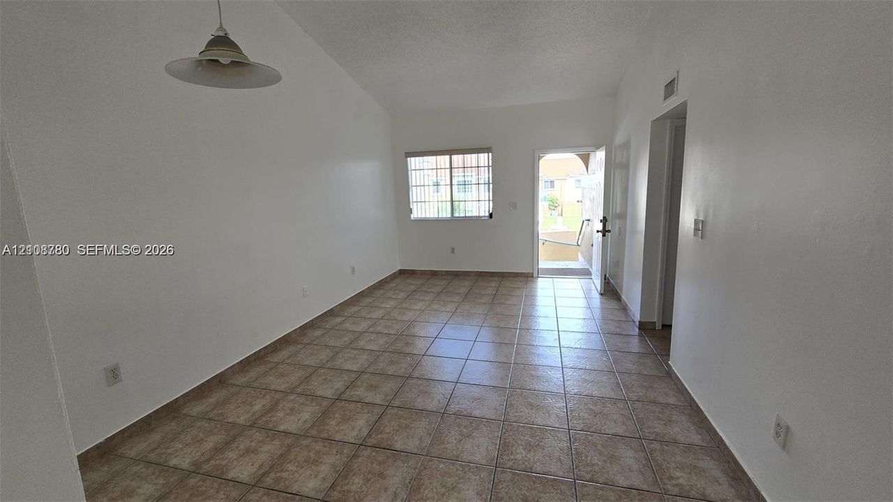 Interior space featuring vaulted ceilings, ceramic tile flooring, a window with security bars, and a pendant light fixture