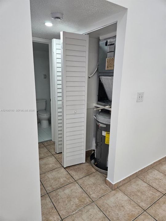 Utility closet featuring louvered bi-fold doors, housing a water heater and HVAC air handler, finished with tile flooring