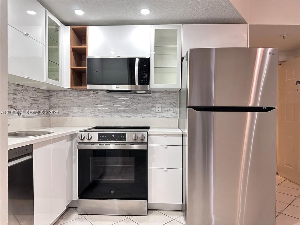 High-gloss white cabinetry featuring open shelving and glass-front upper cabinets, stainless steel appliances, stone-surface countertops, and a textured tile backsplash