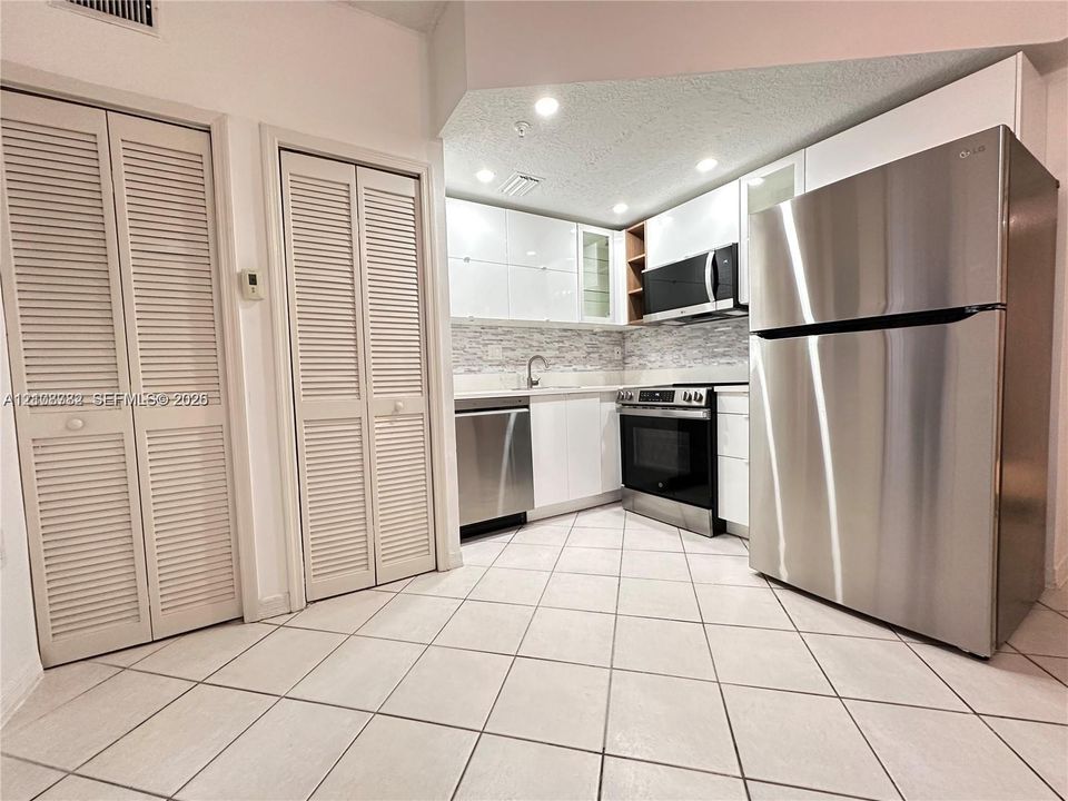 Kitchen featuring white high-gloss cabinetry, stainless steel appliances, a textured stone backsplash, and neutral tile flooring