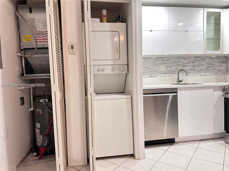 Kitchen featuring high-gloss white cabinetry, stainless steel dishwasher, mosaic tile backsplash, and stacked laundry unit