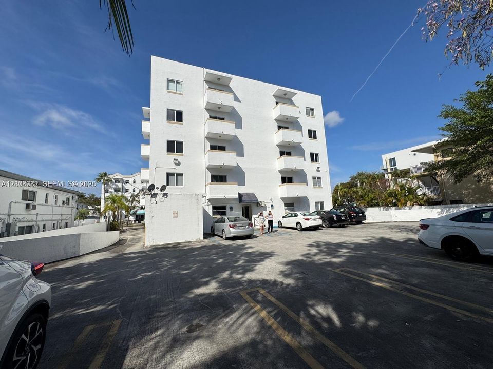 Multi-story white stucco exterior featuring stacked private balconies and dedicated on-site surface parking