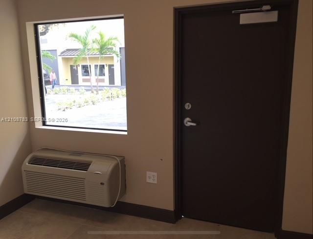 Interior space featuring a large fixed-pane window, a dark-toned solid door with an overhead hydraulic closer, and a wall-mounted climate control unit