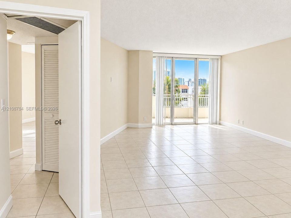 Open-concept room featuring light-colored ceramic tile flooring, floor-to-ceiling glass sliding doors, a metal-railed balcony, and louvered bifold closet doors