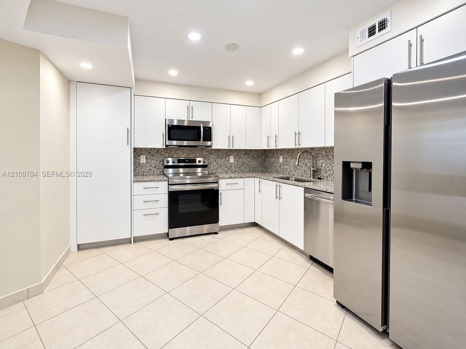 Kitchen featuring white cabinetry, stone-finish countertops, stainless steel appliances, a double-basin undermount sink, and tile flooring