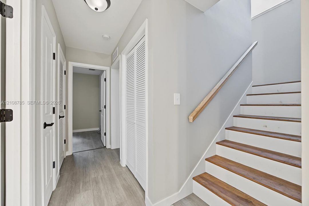 Staircase featuring wood-finish treads and a natural wood handrail, paired with interior doors showcasing matte black hardware and white louvered closet doors