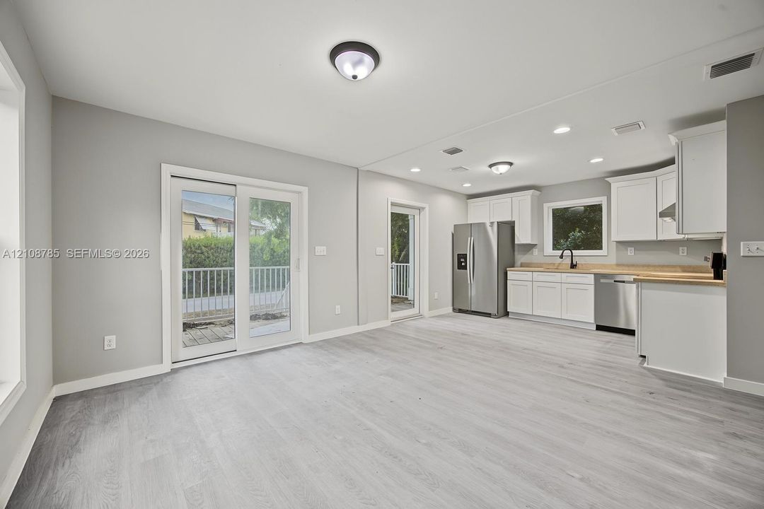 Open-concept space featuring wood-finish flooring, white shaker cabinetry, stainless steel appliances, neutral wall color, and glass sliding door access