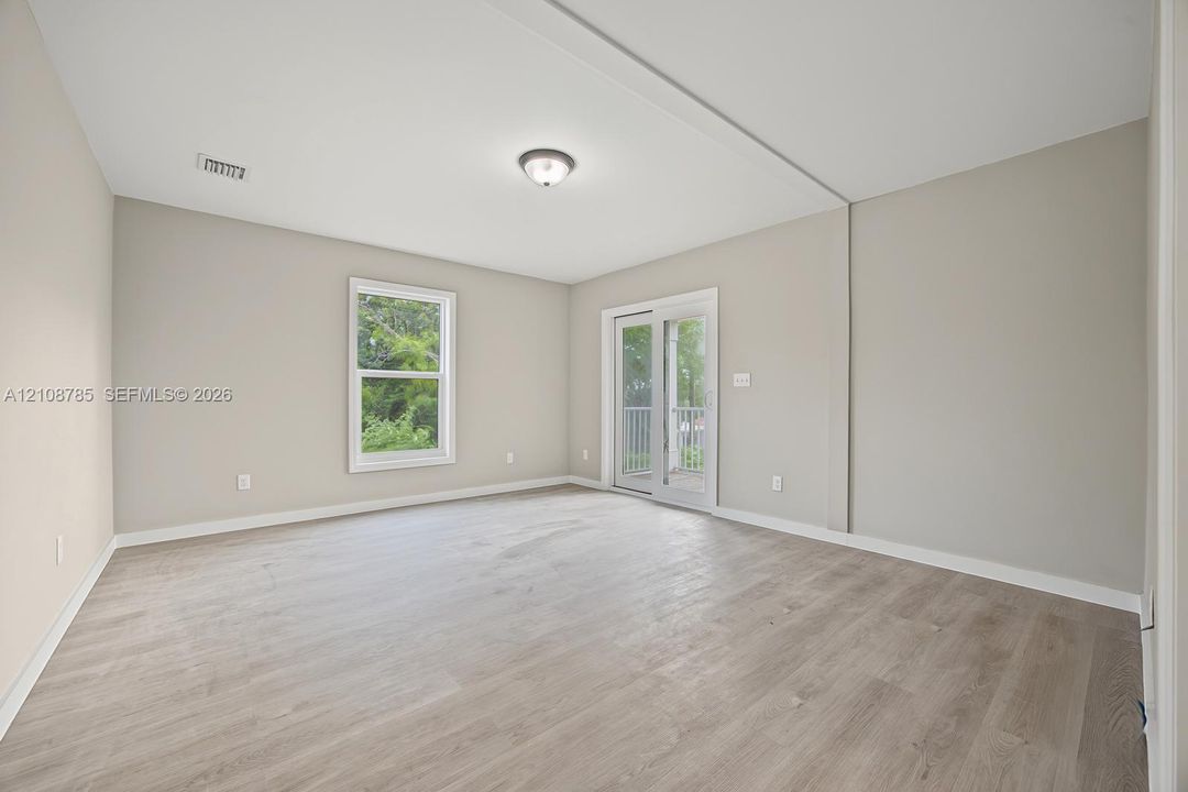 Neutral-toned interior featuring wood-finish flooring, a glass-pane sliding door with exterior access, a single window, and a flush-mount ceiling light fixture