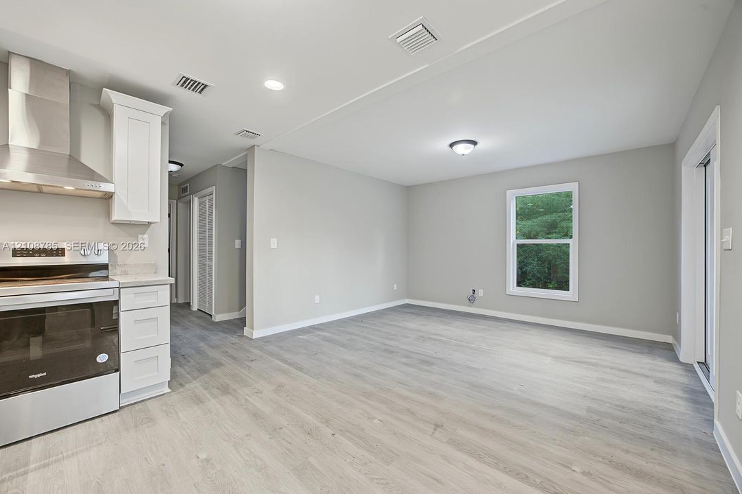 Kitchen featuring stainless steel range, professional-grade range hood, white cabinetry, and wood-finish flooring