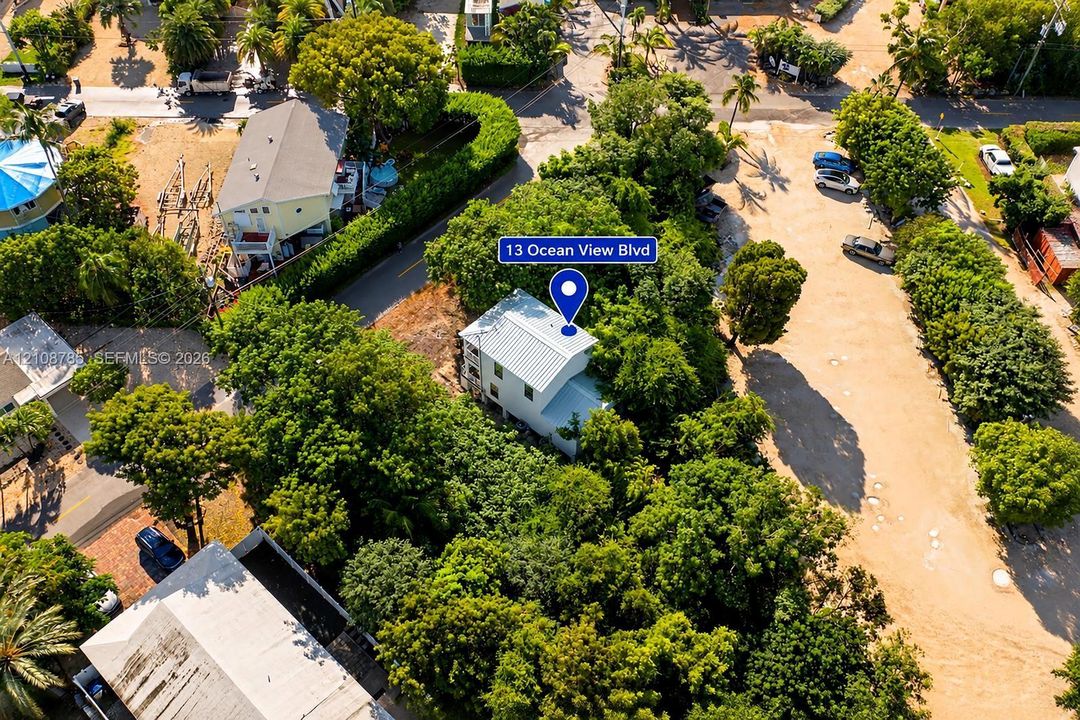 Aerial perspective of a multi-story residence featuring a metal roof, nestled within a lot characterized by mature tree canopy and established vegetation