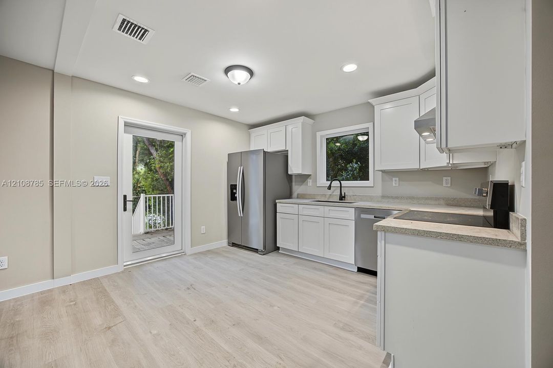 Kitchen featuring white cabinetry, stone-finish countertops, stainless steel appliances, a deep-basin sink with a matte black faucet, and wood-finish flooring