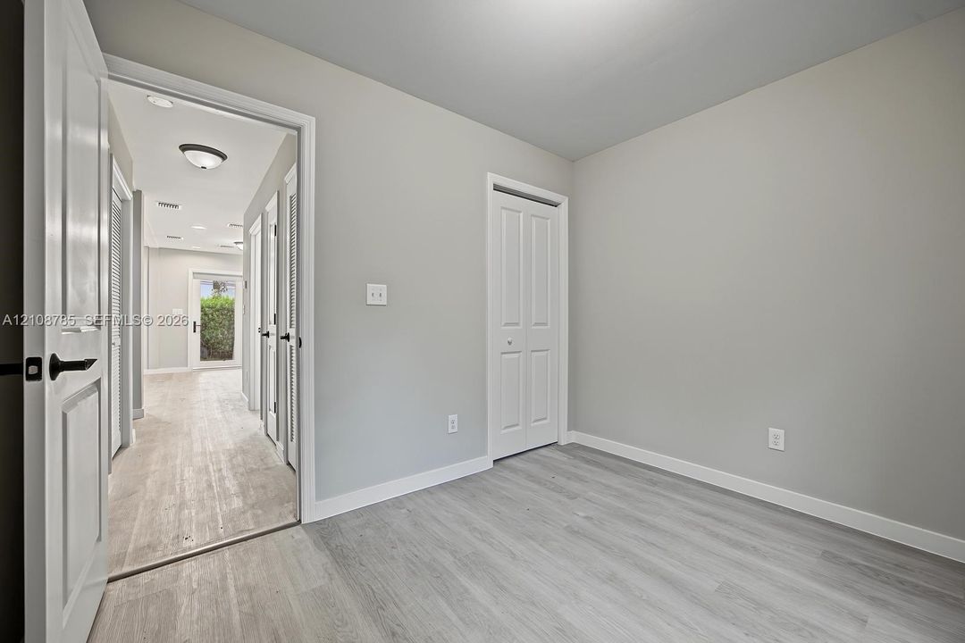 Interior space featuring neutral-toned walls, wood-finish flooring, and white paneled doors with matte black hardware