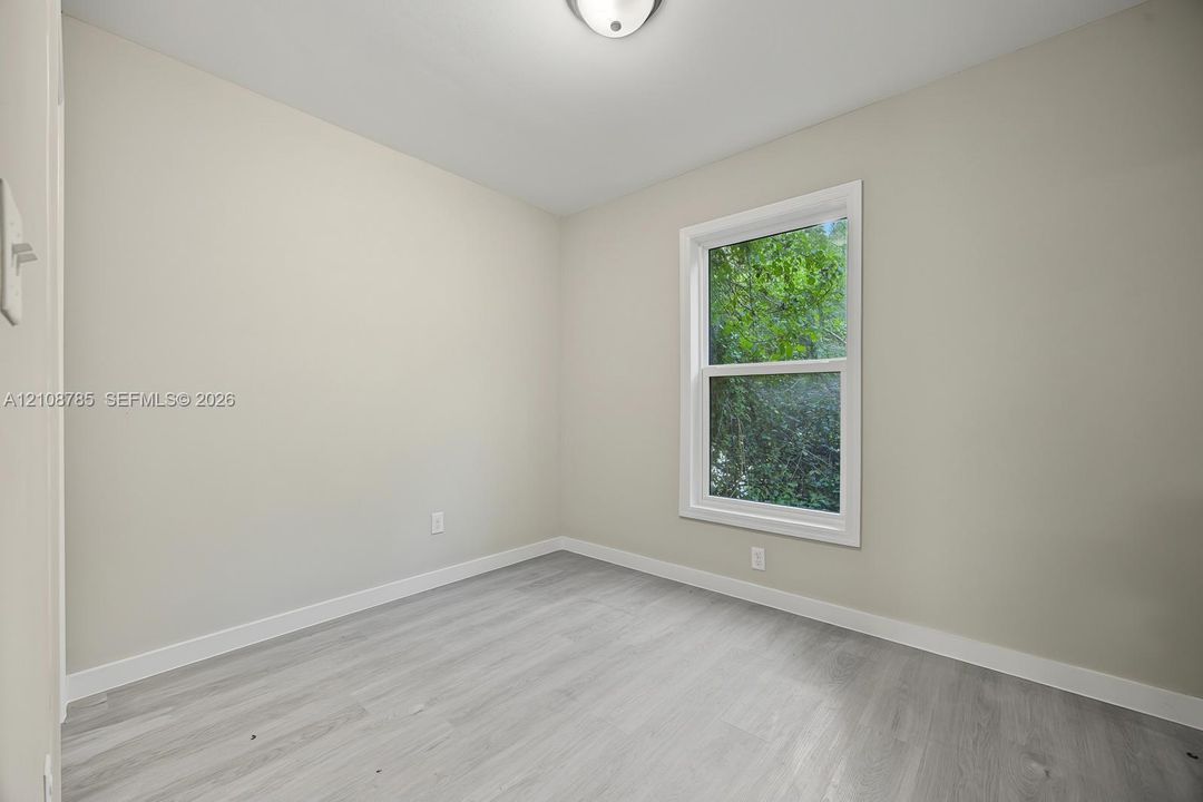 Neutral-toned walls, wood-finish flooring, and a double-hung window with a verdant exterior outlook, illuminated by a ceiling-mounted light fixture
