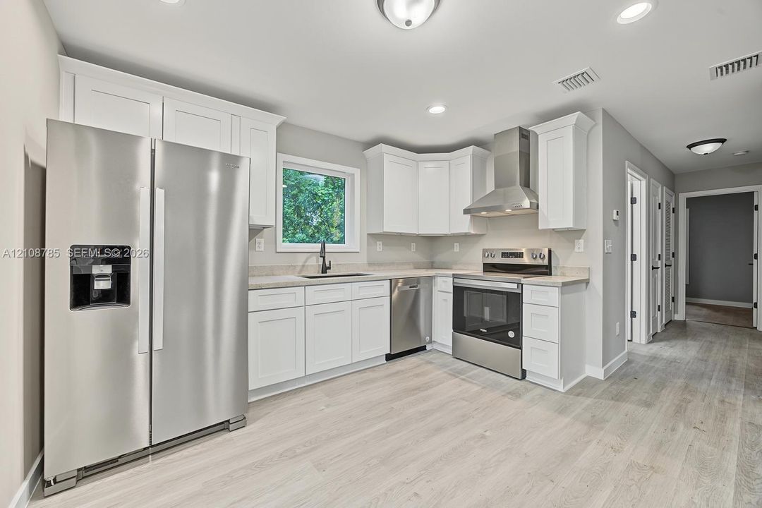 Kitchen featuring white shaker-style cabinetry, stainless steel appliances, a stainless steel range hood, stone-finish countertops, and wood-finish flooring