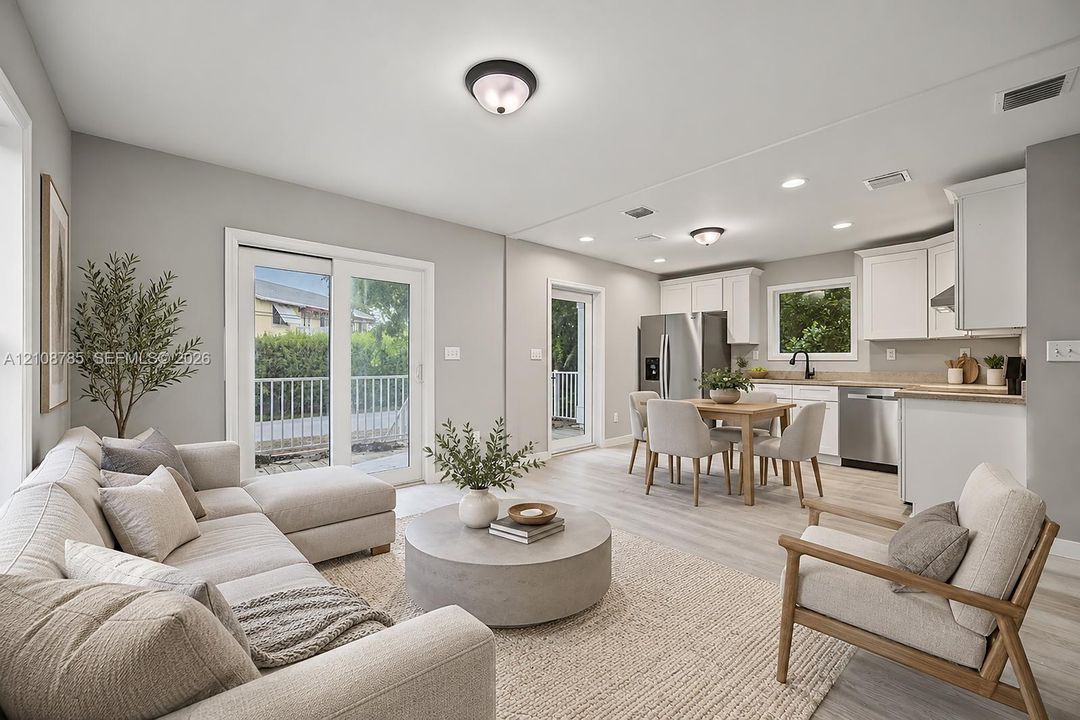 Open-concept living space featuring wood-finish flooring, white cabinetry, stainless steel appliances, recessed lighting, and glass sliding doors