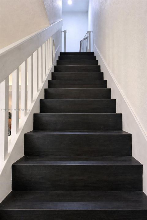 Staircase featuring dark-stained wood treads, contrasting white handrail, and white vertical balusters