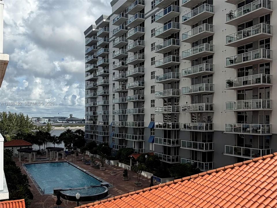 Multi-story residential building featuring private balconies with glass railings, outdoor swimming pool, terracotta-style roof tiles, and manicured landscaping