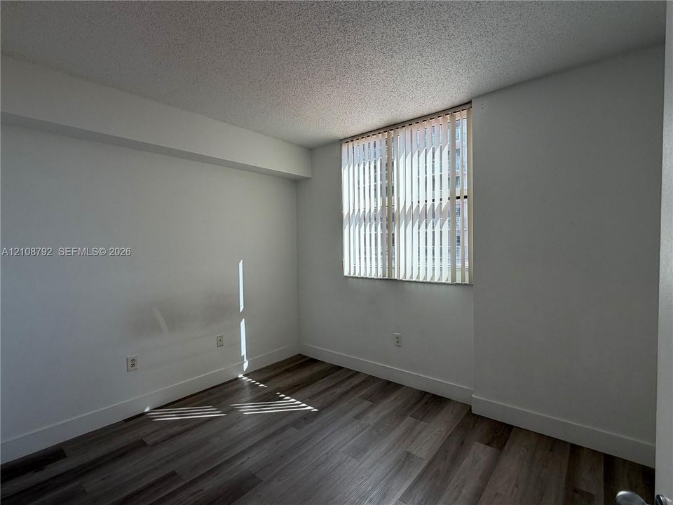 Room featuring wood-finish flooring, neutral walls, and a large window with vertical blinds