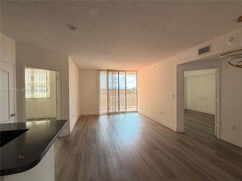 Living area featuring wood-finish flooring, floor-to-ceiling sliding glass doors, dark-toned countertop, and recessed ceiling lighting