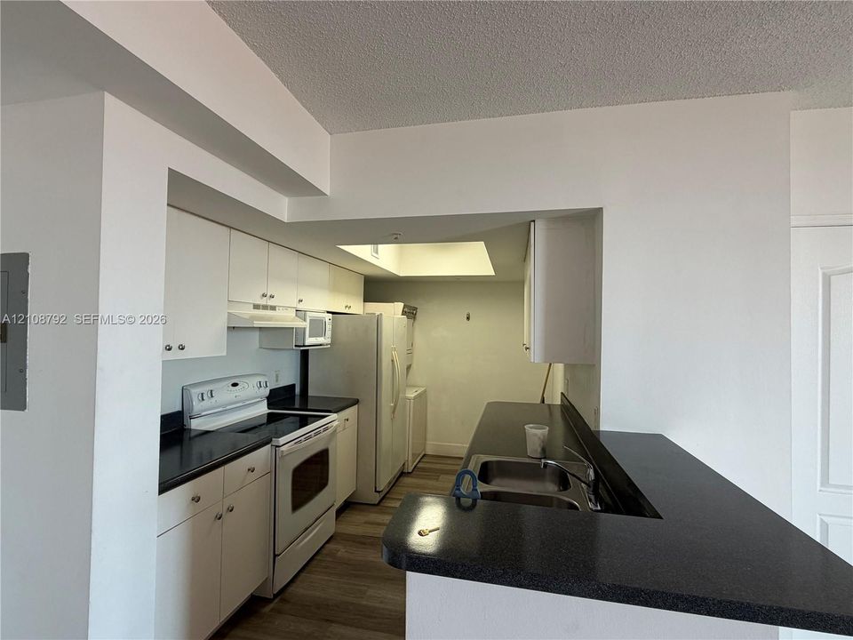 Kitchen featuring white cabinetry, dark countertops, a double-basin stainless steel sink, built-in range, and wood-finish flooring