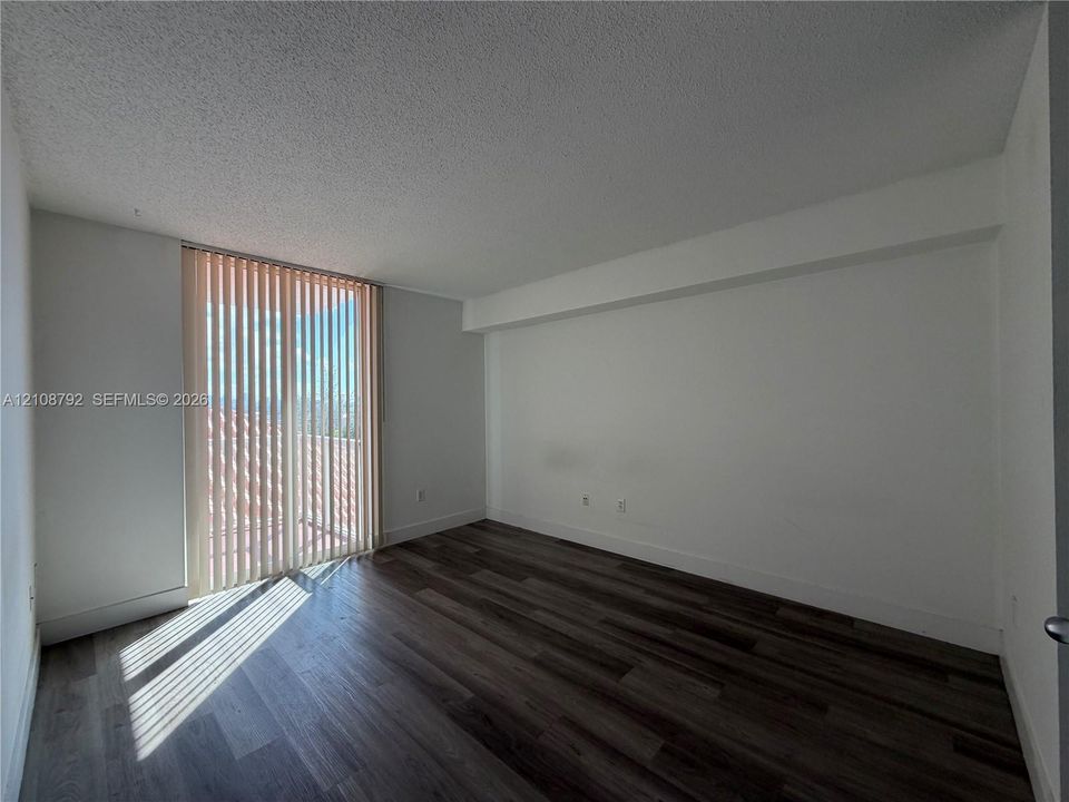 Interior space featuring wood-finish flooring, white walls, and a glass sliding door with vertical blinds