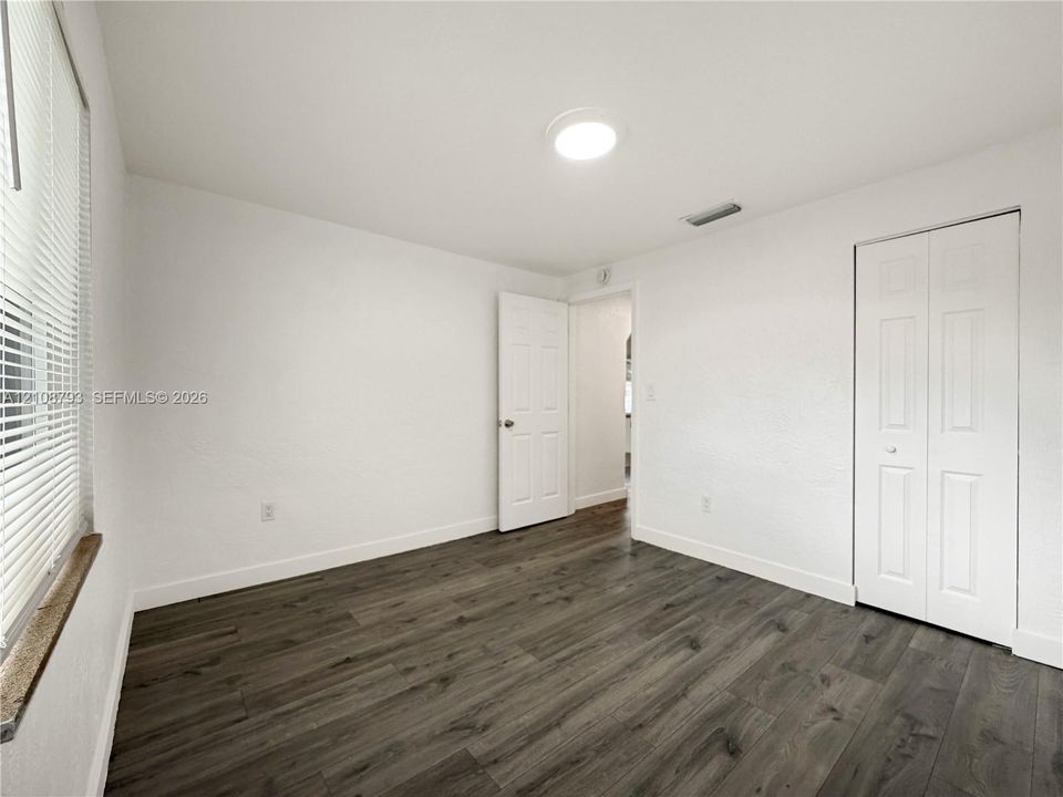 Room featuring wood-finish flooring, crisp white walls, flush-mount ceiling lighting, and a bi-fold closet door