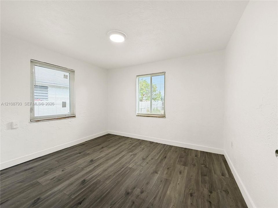 Room featuring wood-finish flooring, two windows with blinds, and a flush-mount ceiling light fixture
