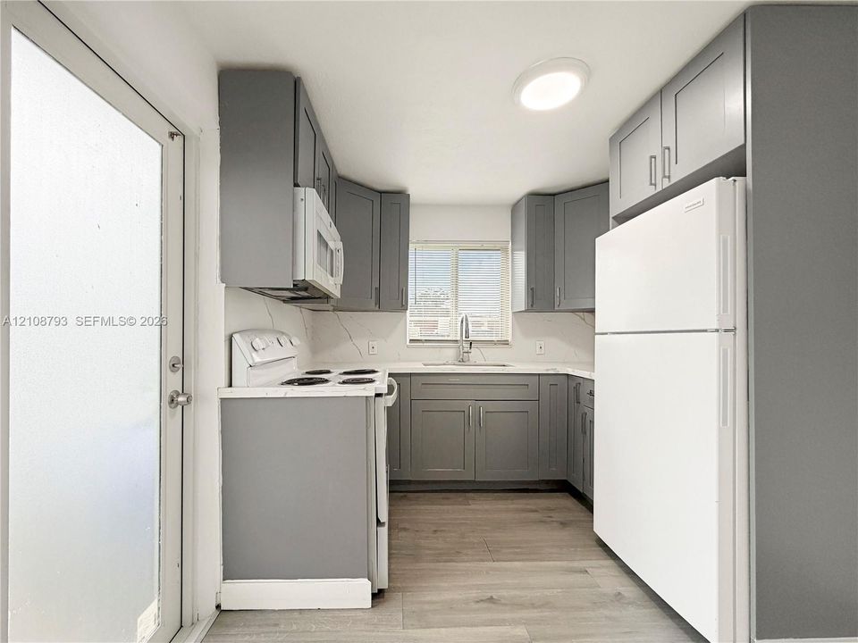 Kitchen featuring grey shaker-style cabinetry, solid-surface countertops with backsplash, wood-finish flooring, and white appliances
