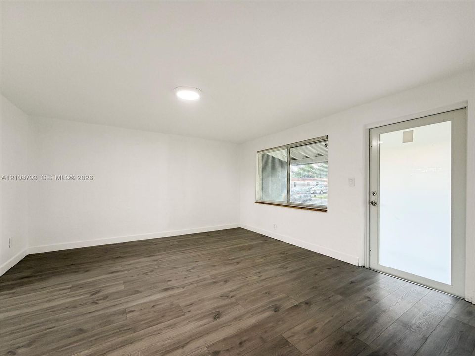 Neutral interior featuring wood-finish flooring, white walls, a flush-mount ceiling light, a single-pane horizontal window, and a glass-panel entry door