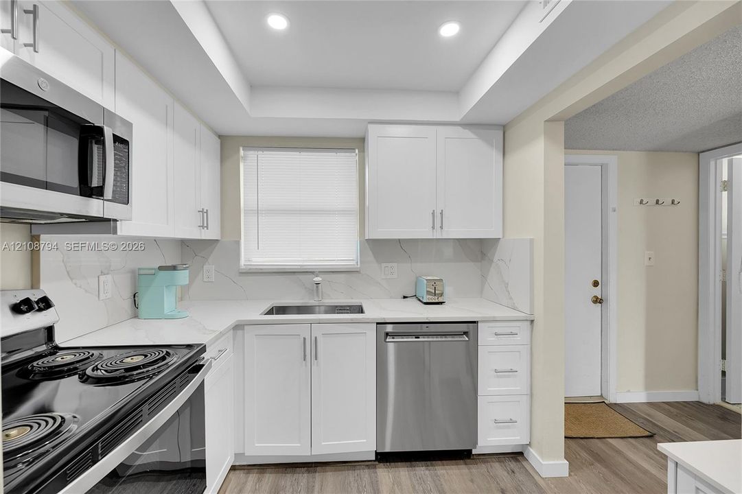 Kitchen featuring white shaker-style cabinetry, solid-surface countertops with matching backsplash, stainless steel appliances, and wood-finish flooring