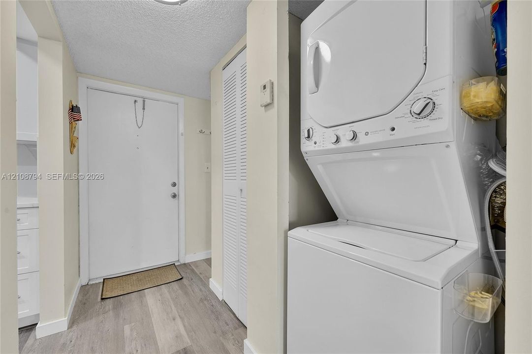 Laundry area featuring a stackable washer and dryer, wood-finish flooring, and a louvered bi-fold closet door