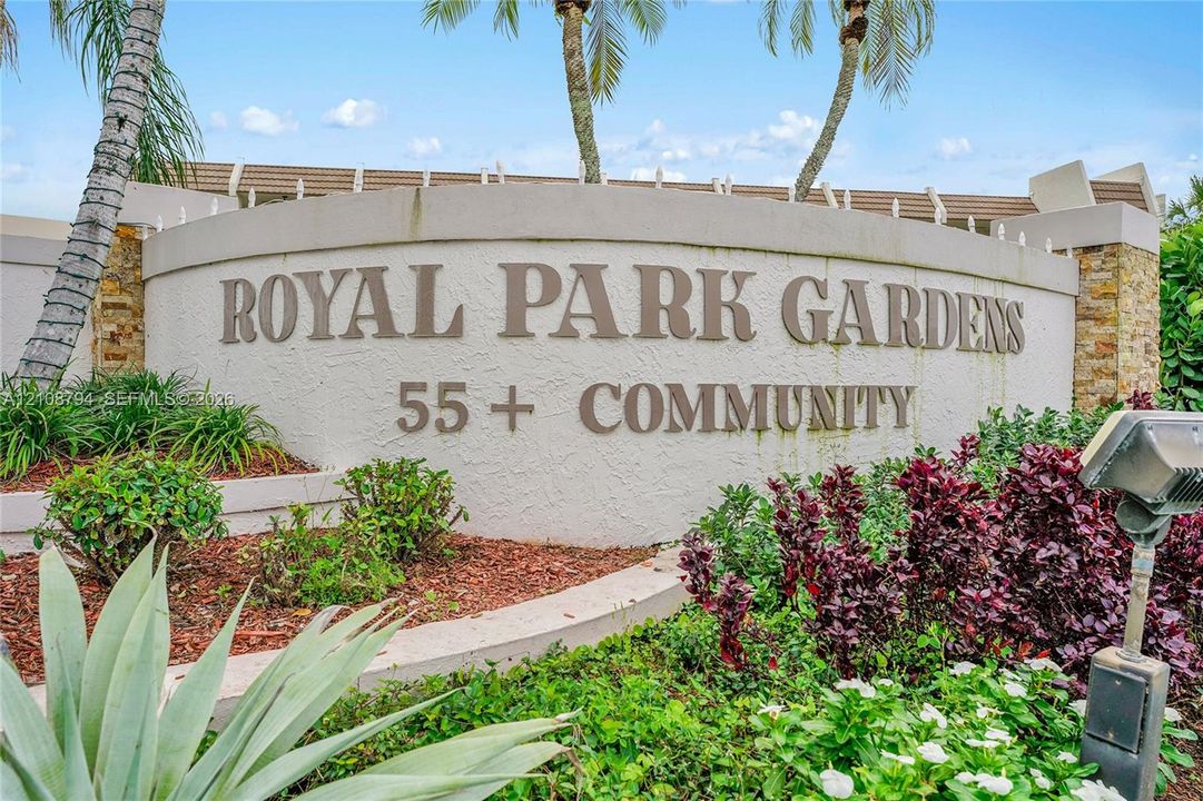Stucco community entrance monument featuring stone-accented pillars, integrated landscaping, and palm trees