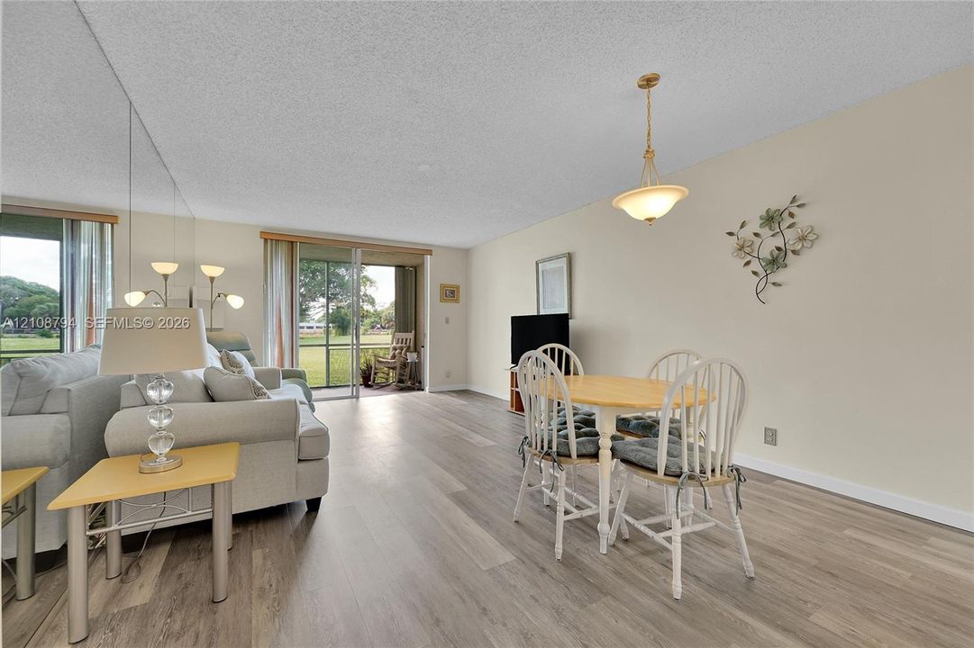 Living area featuring wood-finish flooring, floor-to-ceiling mirrored wall, and sliding glass doors with access to a screened patio