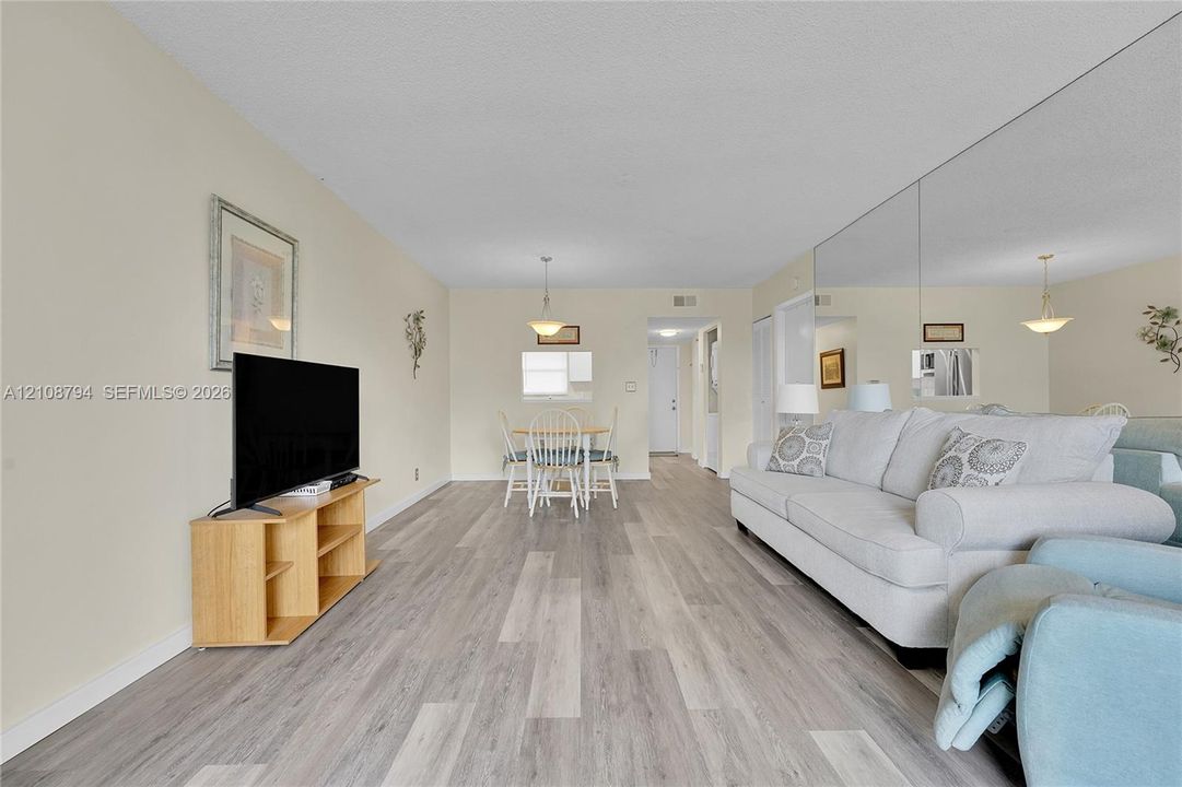 Living area featuring wood-finish flooring, floor-to-ceiling mirrored wall, and overhead pendant lighting