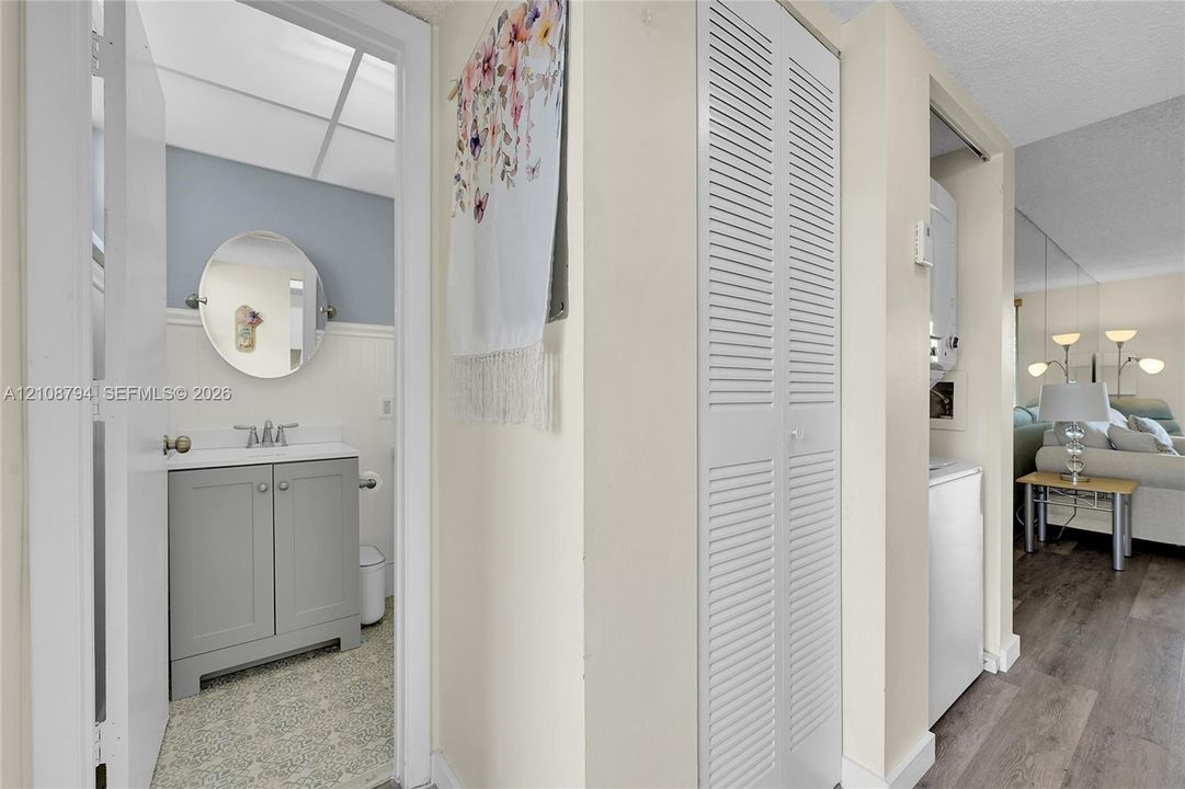 Bathroom featuring a gray vanity with a white countertop, oval mirror, white beadboard wainscoting, and patterned floor tile, complemented by a laundry closet with white louvered doors