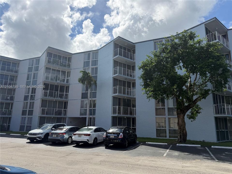 Multi-story structure featuring a light-toned exterior, stacked screened balconies, floor-to-ceiling windows, and dedicated asphalt surface parking