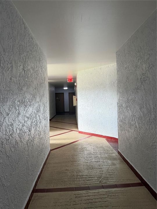 Interior hallway featuring textured wall finishes, tile flooring with decorative inlay, and flat-surface ceilings