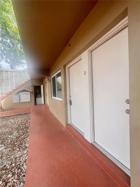 Covered exterior walkway featuring solid-core white doors, concrete-finish flooring, and wall-mounted mailboxes