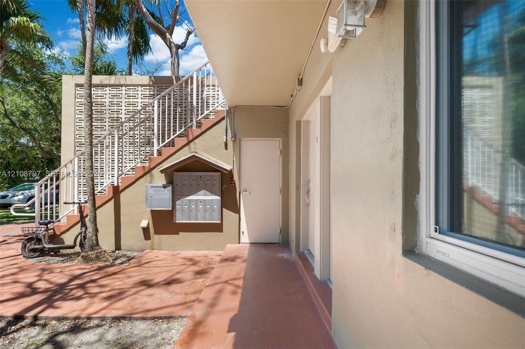 Covered entryway featuring a concrete walkway, decorative concrete screen wall, exterior staircase with metal railing, and wall-mounted metal mailboxes