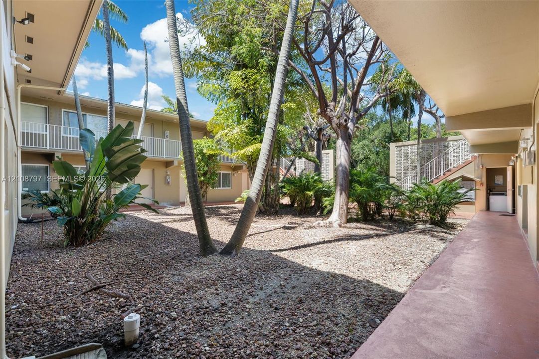 Central courtyard featuring mature palm and hardwood trees, gravel ground cover, established landscaping, and covered exterior walkways with metal railings