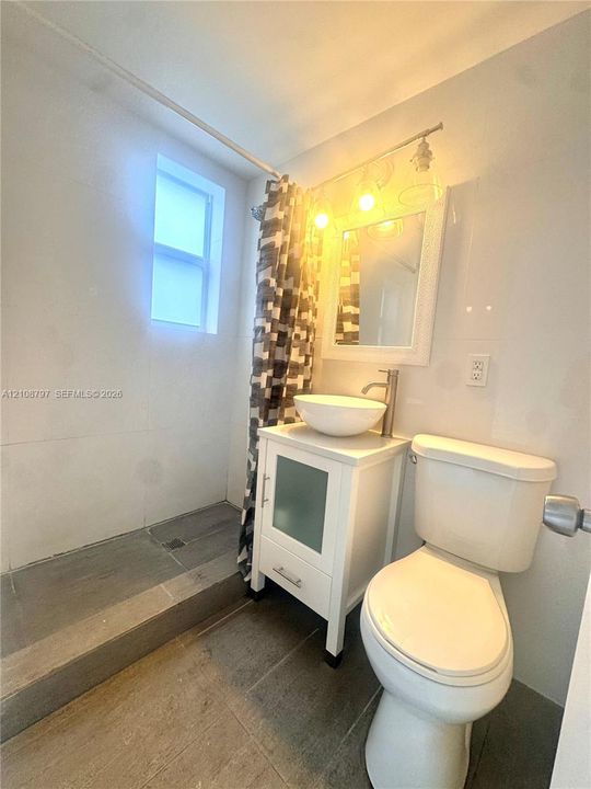Bathroom featuring stone-finish flooring, a white vanity cabinet with a vessel sink, a single-handle faucet, and a wall-mounted mirror