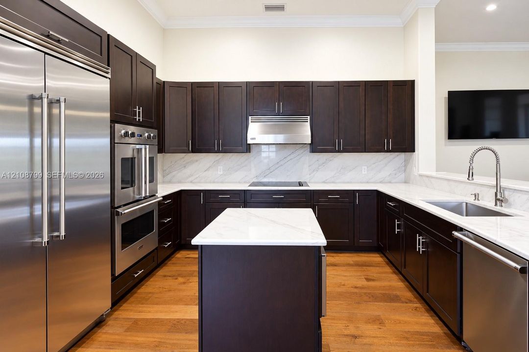 Kitchen featuring dark wood cabinetry, a central island with a stone countertop, stone slab backsplash, stainless steel appliances, and wood-finish flooring
