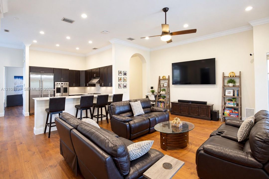 Open concept interior featuring wood-finish flooring, recessed lighting, crown molding, and a kitchen with dark cabinetry and a breakfast bar